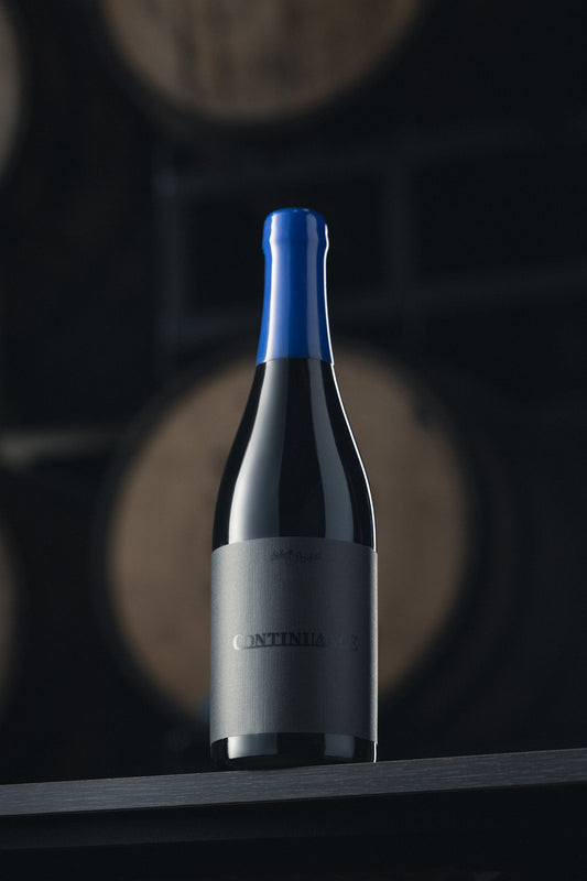 Beer bottle with blue wax cap on a wooden surface with barrels in the background