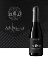 Black beer bottle labeled 'The Blend' with Topping Goliath Brewing Co. and Side Project logos on a dark background.