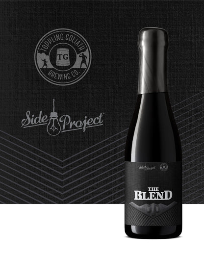 Black beer bottle labeled 'The Blend' with Topping Goliath Brewing Co. and Side Project logos on a dark background.